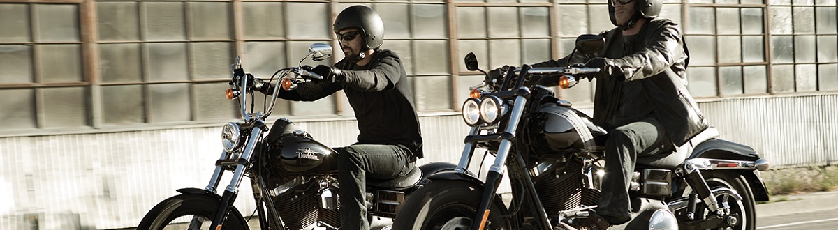 Two men riding Harley-Davidson® motorcycles in the city with warehouse windows in the background